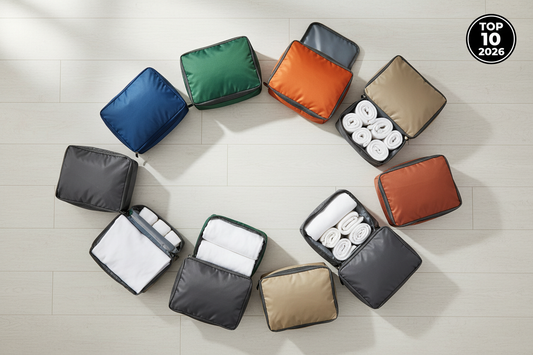 10 cubes de rangement de voyage en flat lay, chacun d'une couleur distincte (bleu, vert, orange, gris, beige, terracotta), certains ouverts avec des vêtements pliés