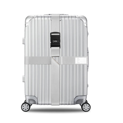 Sangle pour valise croisée antivol à code fixée sur une valise rigide argent, utilisée en situation réelle dans un aéroport, avec poignée télescopique tirée par un voyageur. gris